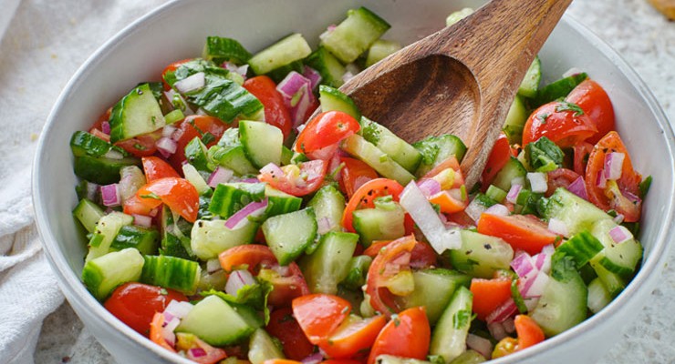 spooning fresh israeli salad in bowl bowl of salad
